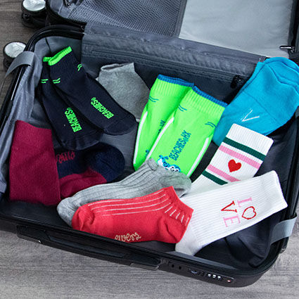 Geöffneter Koffer mit Beachies, Sneakersocken, Stricksocken, Tennissocken, Basicsocken. Packliste für den Urlaub/Ratgeber Sommerpackliste.