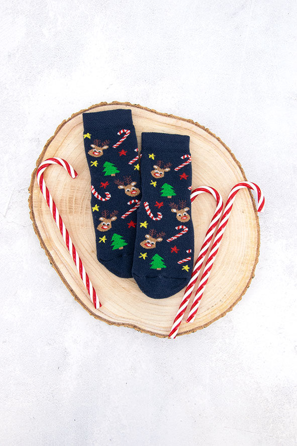 Weihnachtssocken dunkelblau/marine/navy mit Motiv Zuckerstangen, Rentier, Sterne und Weihnachtsbäume in bunten Farben liegen auf einem Baumstamm. Daneben liegen Zuckerstangen in rot/weiß. Der Hintergrund ist weiß.