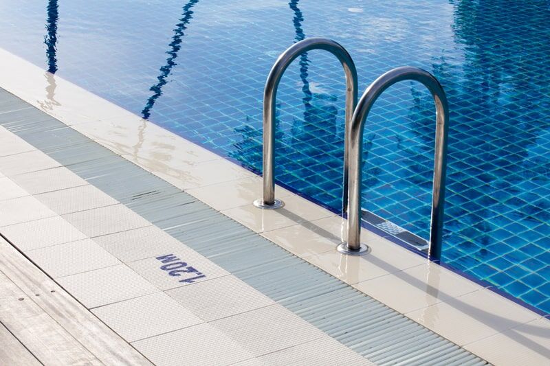 Poolrand mit Edelstahlleiter und Tiefenangabe ‚1.20M' auf blauem Fliesenbecken