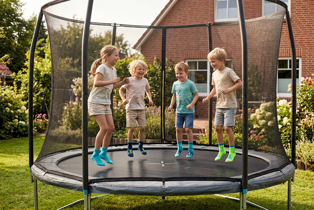 Vier lachende Kinder in bunten BEACHIES® Socken springen gemeinsam auf einem Trampolin in einem sommerlichen Garten